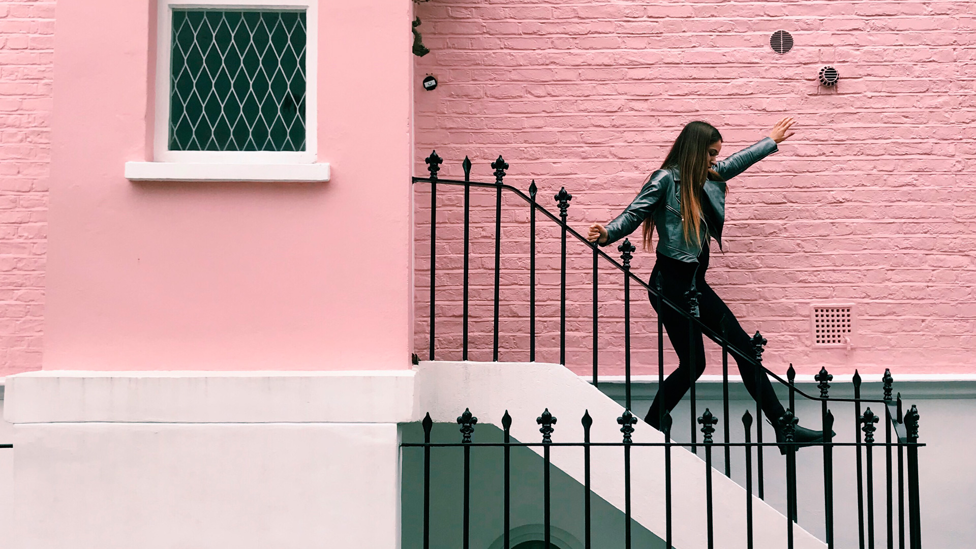 uma casa rosa de alvenaria e uma menina descendo as escadas
