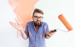 Homem confuso com termos de pintura enquanto tenta pintar a parede com tinta laranja